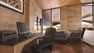 A modern office space with wooden walls, a desk with a computer, two office chairs, and large windows offering a view of the outdoors.