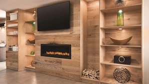 Ein modernes Wohnzimmer mit Flachbildfernseher, Kamin, Holzböden und dekorativen Elementen, sowie ein sichtbarer Küchenbereich links.