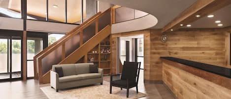 A spacious lobby with a wooden reception desk, a staircase, a sofa, and a bookshelf.