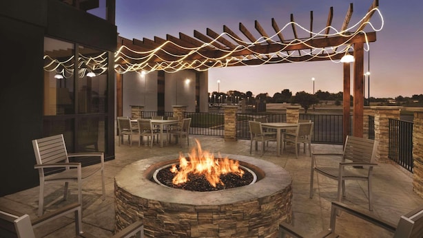 Ein Patio im Freien mit einem Steinkamin, Sitzgelegenheiten und einer Pergola mit Lichterketten.