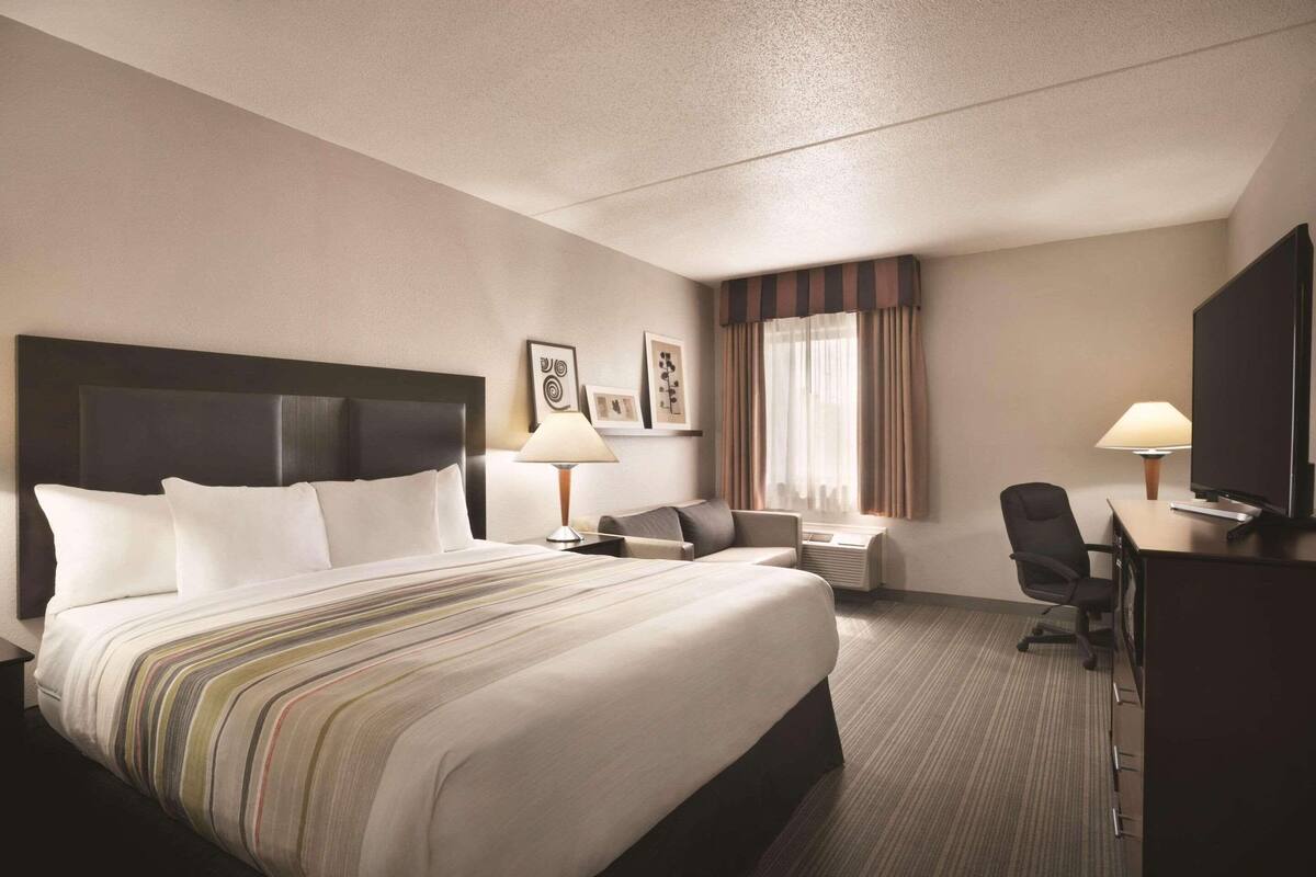 Ein Hotelzimmer mit einem großen Bett, zwei Nachttischen mit Lampen, einem Schreibtisch mit Stuhl und einem Fernseher.