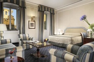 Camera d'albergo con un letto, due poltrone, un tavolino con una bevanda e vista su un edificio storico.