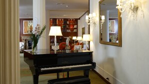 Un piano à queue dans une pièce bien éclairée, avec un grand miroir et une bibliothèque remplie de livres.