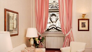 Une chambre élégamment aménagée, dotée d’un canapé, de fauteuils, d’une table à manger où le petit-déjeuner est servi, et offrant une vue agréable par la fenêtre.