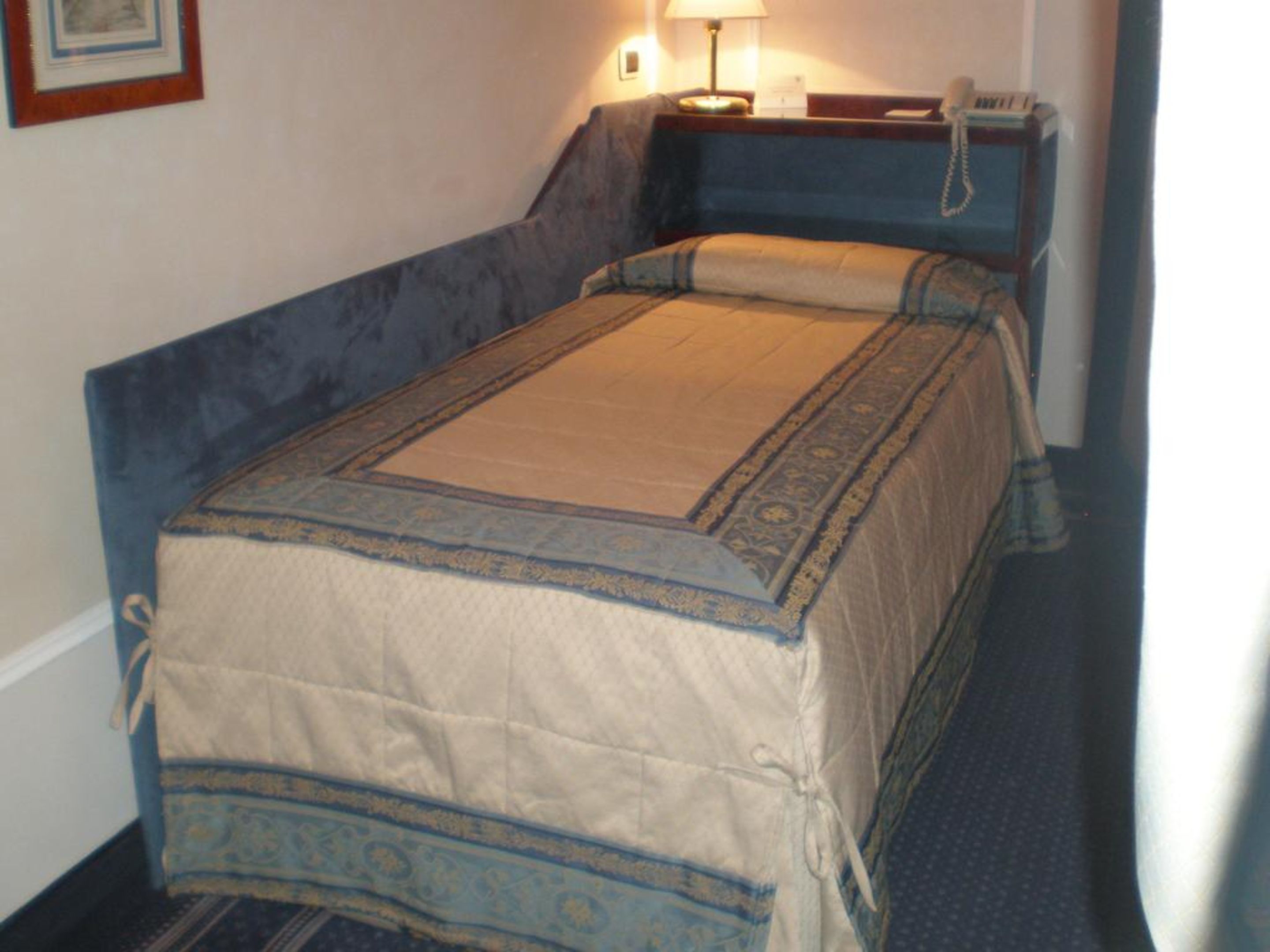 Een enkel bed met een blauw hoofdbord en een beige dekbedovertrek met blauwe rand.