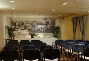 Una sala conferenze con file di sedie, un lungo tavolo e un grande murale in bianco e nero raffigurante un panorama cittadino.