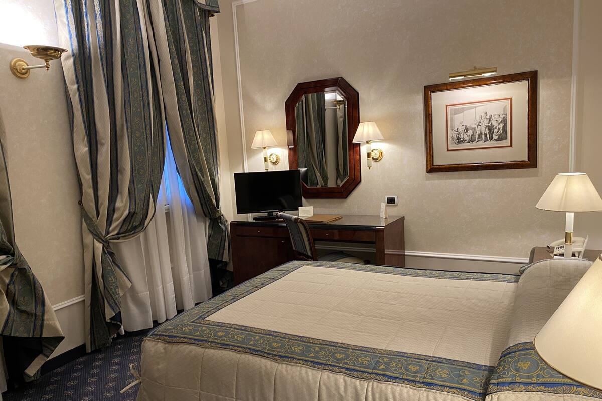 A hotel room with a bed, desk, chair, television, and a framed picture on the wall.