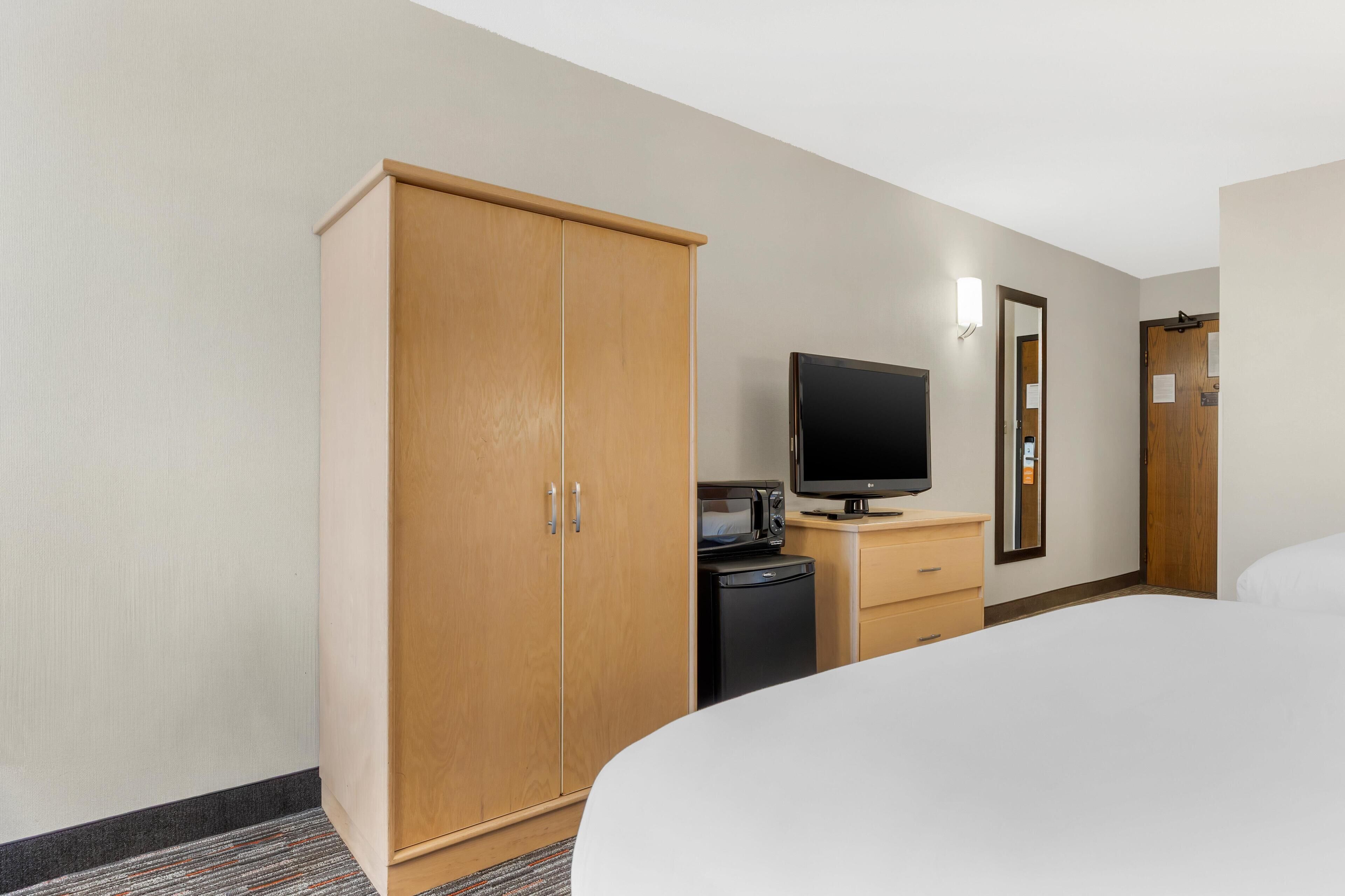 Una camera d'albergo con un letto, un armadio, una televisione, un forno a microonde e un piccolo frigorifero.