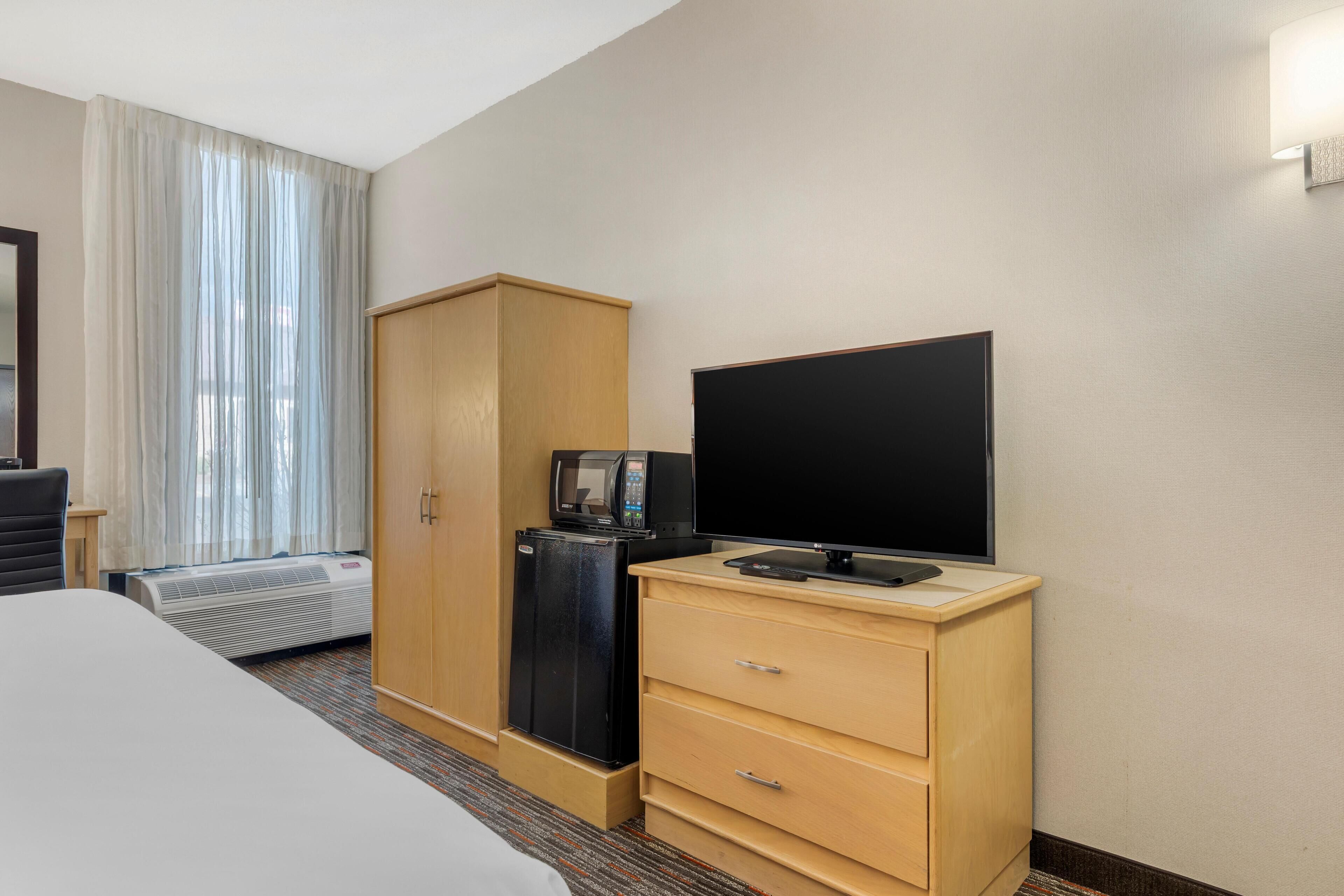 A hotel room with a bed, a wardrobe, a television, a mini-fridge, and a window with curtains.