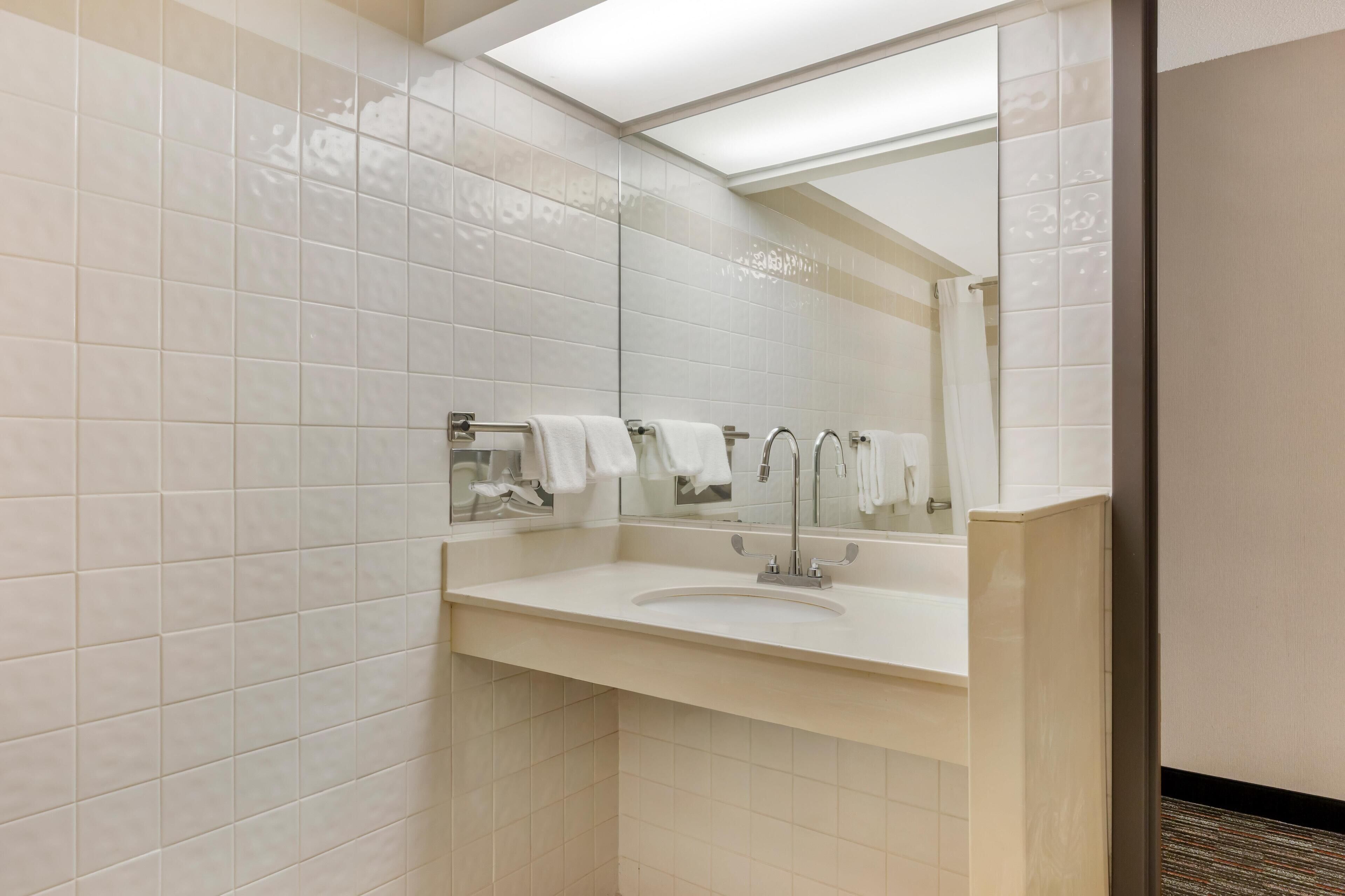 A modern bathroom with white tiles, a sink, and a mirror.