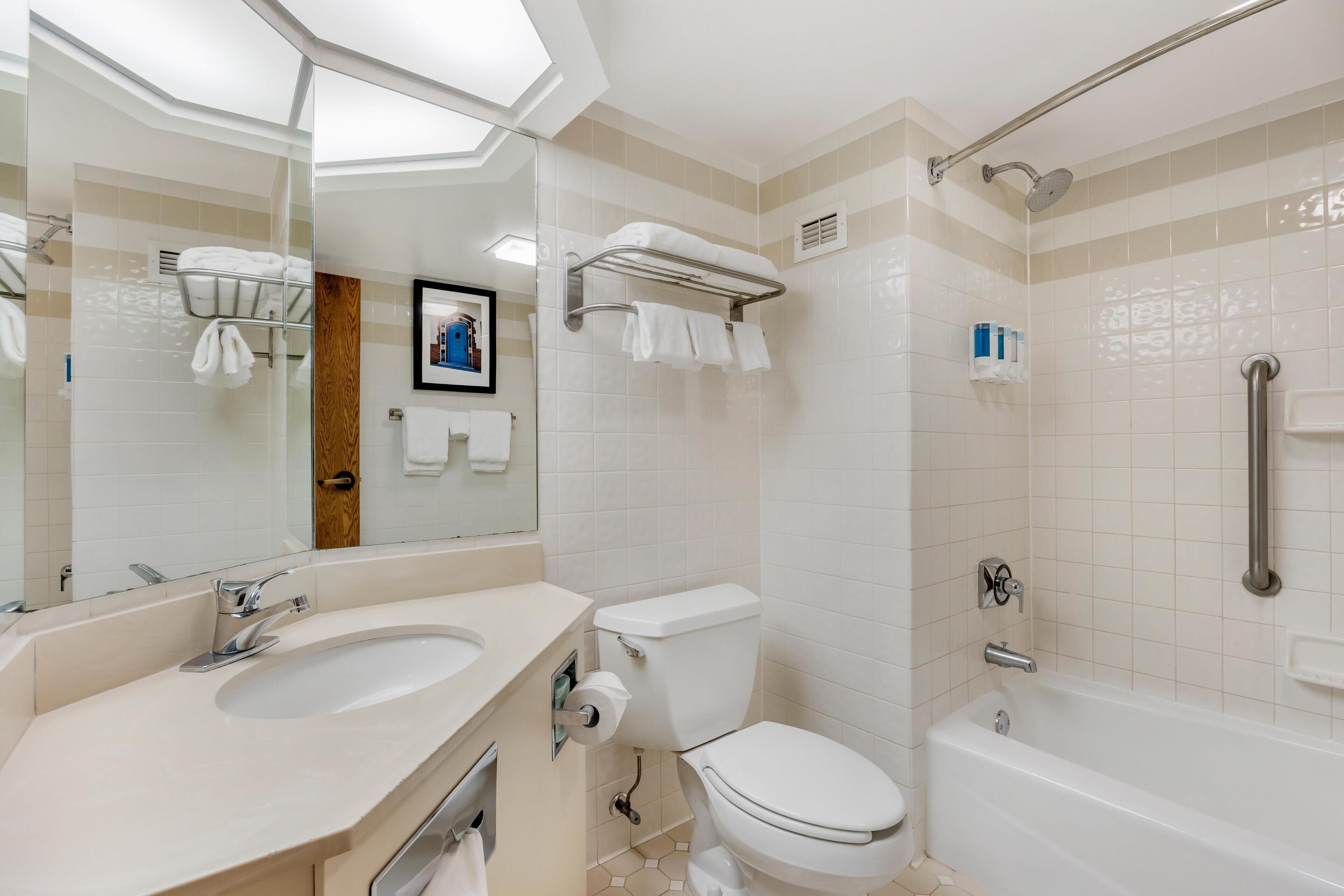 A modern bathroom with a large mirror, two sinks, a toilet, and a bathtub.