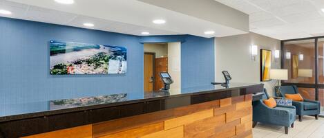 Un área de recepción con un mostrador de madera, una pared azul con una pintura de paisaje y dos sillones azules con cojines naranjas.