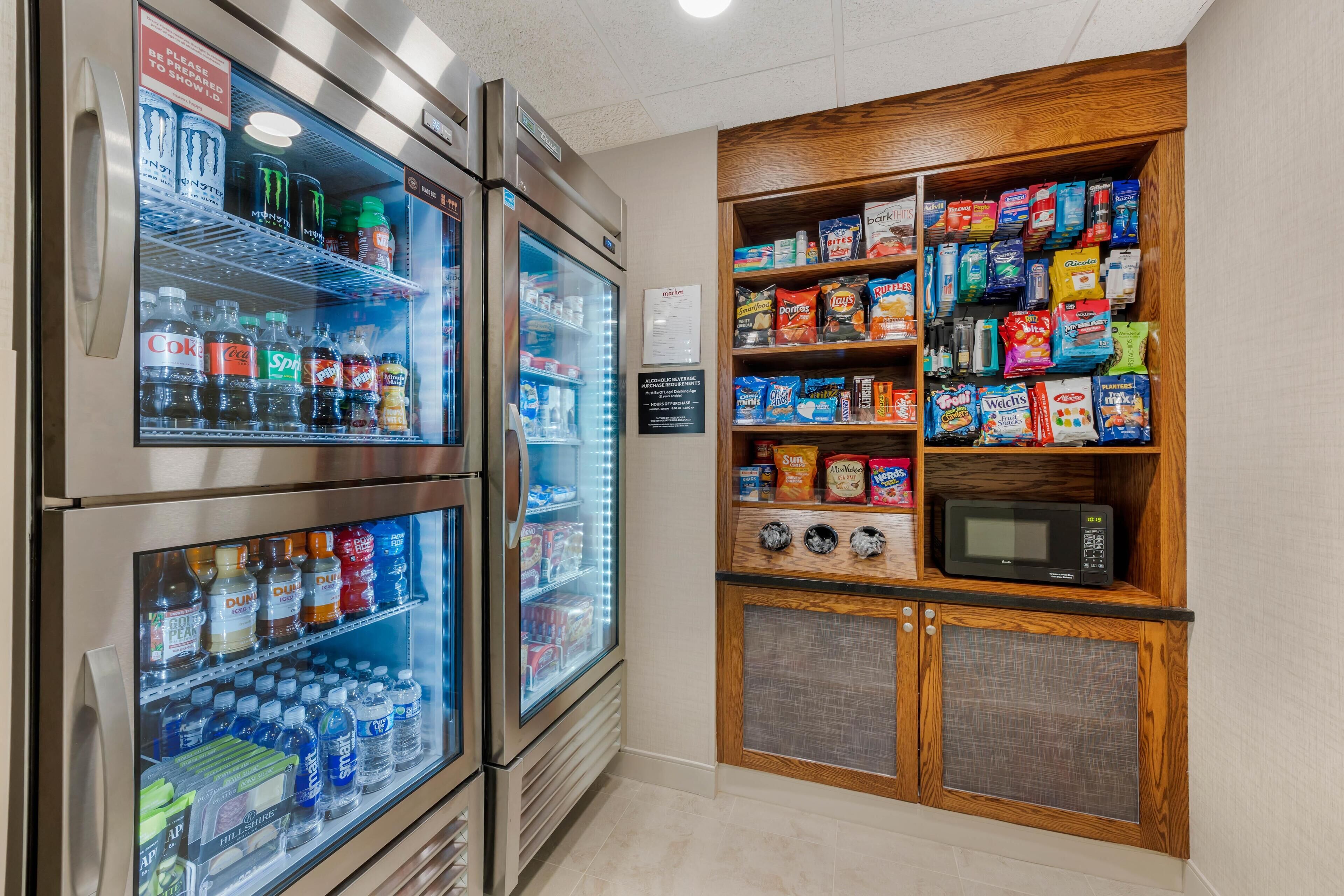 A vending area with refrigerated drinks and snacks, a microwave, and a sign indicating a 24-hour service area.