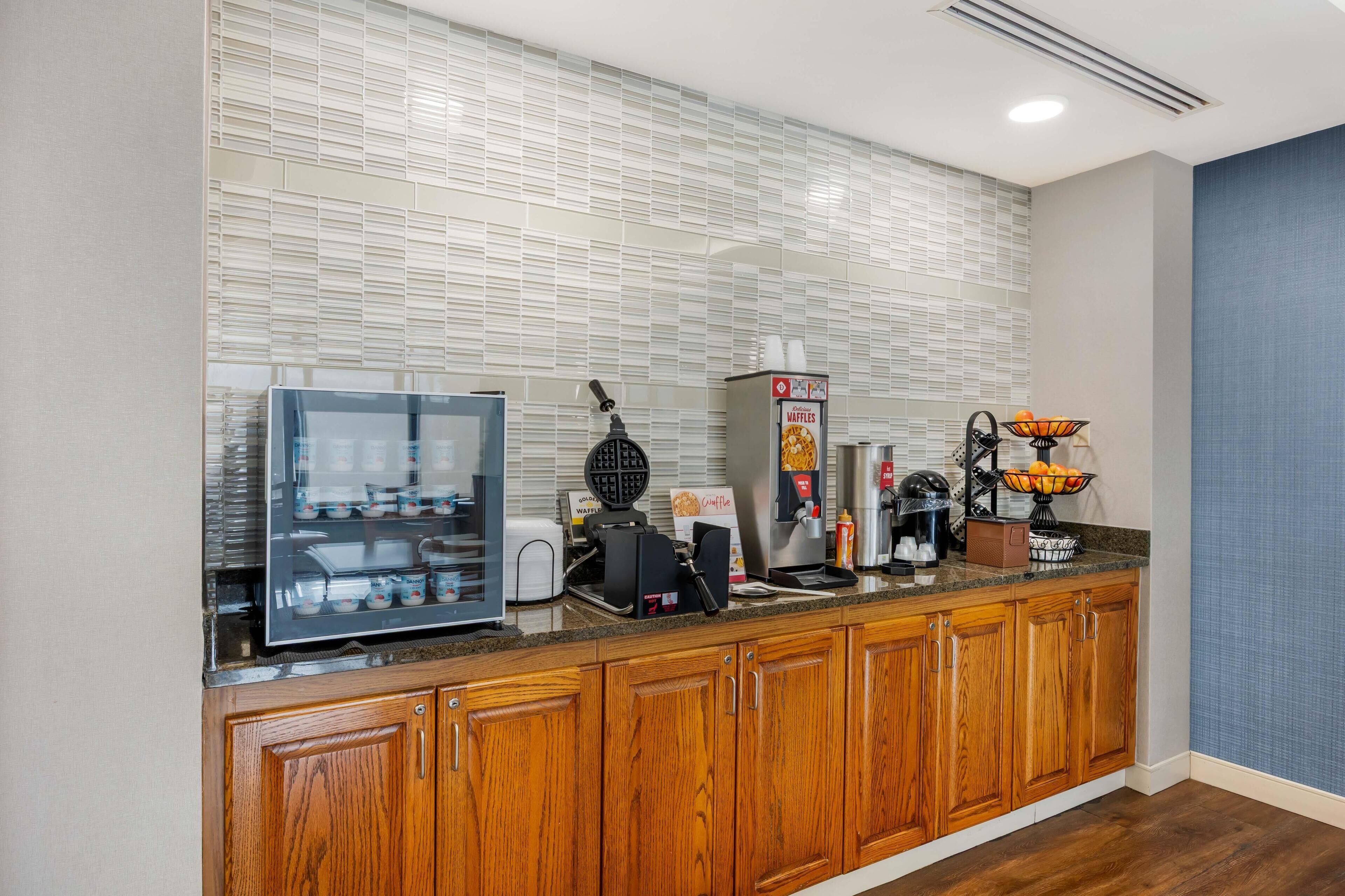 A modern kitchen with a waffle maker, coffee machine, and a display case.