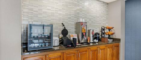 A modern kitchen with a waffle maker, coffee machine, and a display case.