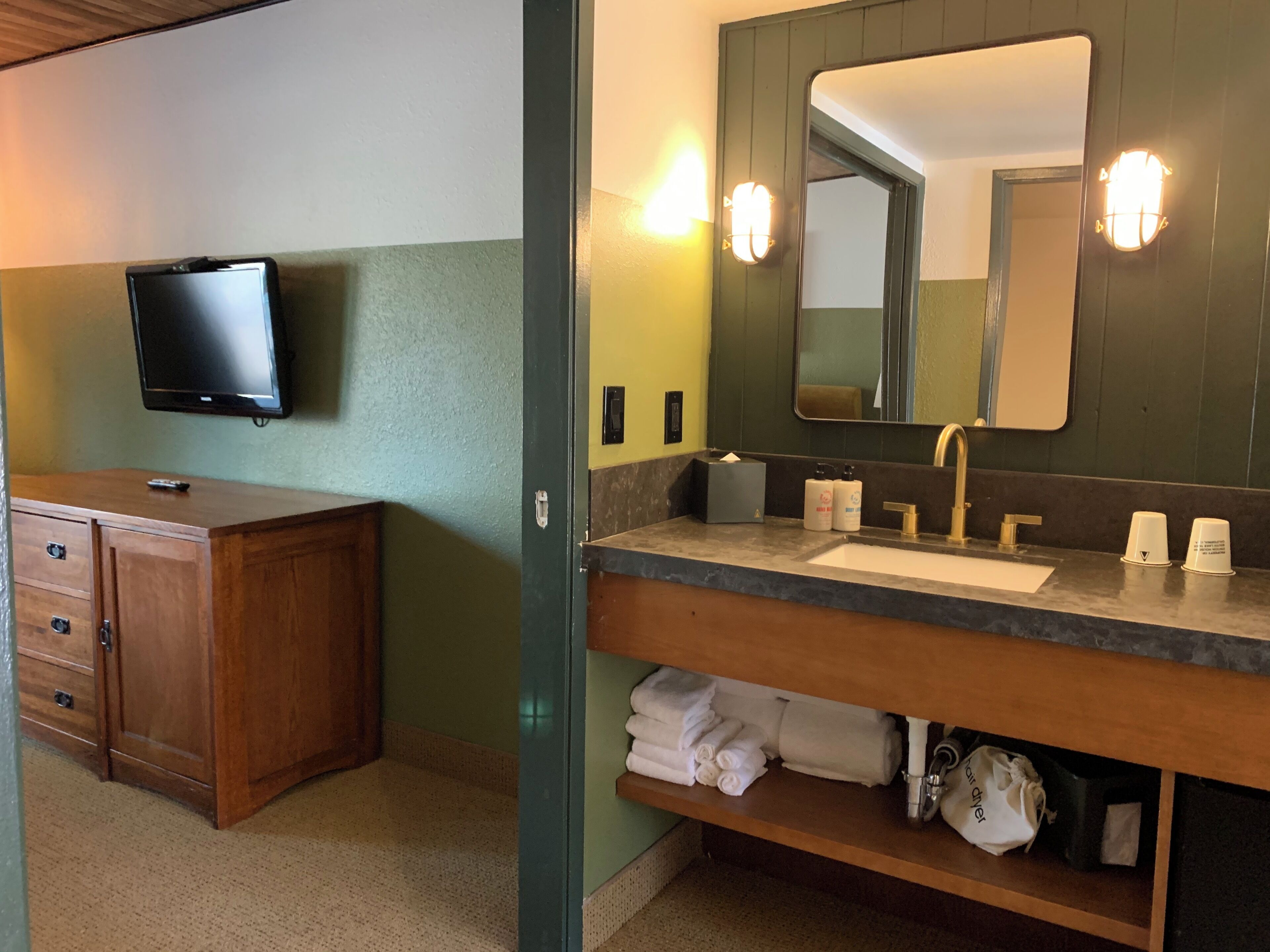 A bathroom with a sink, mirror, towel rack, and a television mounted on the wall.