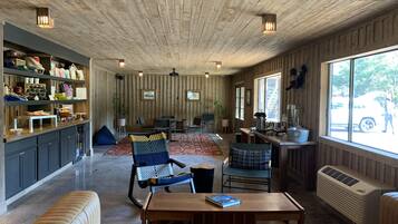 A spacious living area with a wooden ceiling, a sofa, a coffee table, and a kitchen area with a window view.