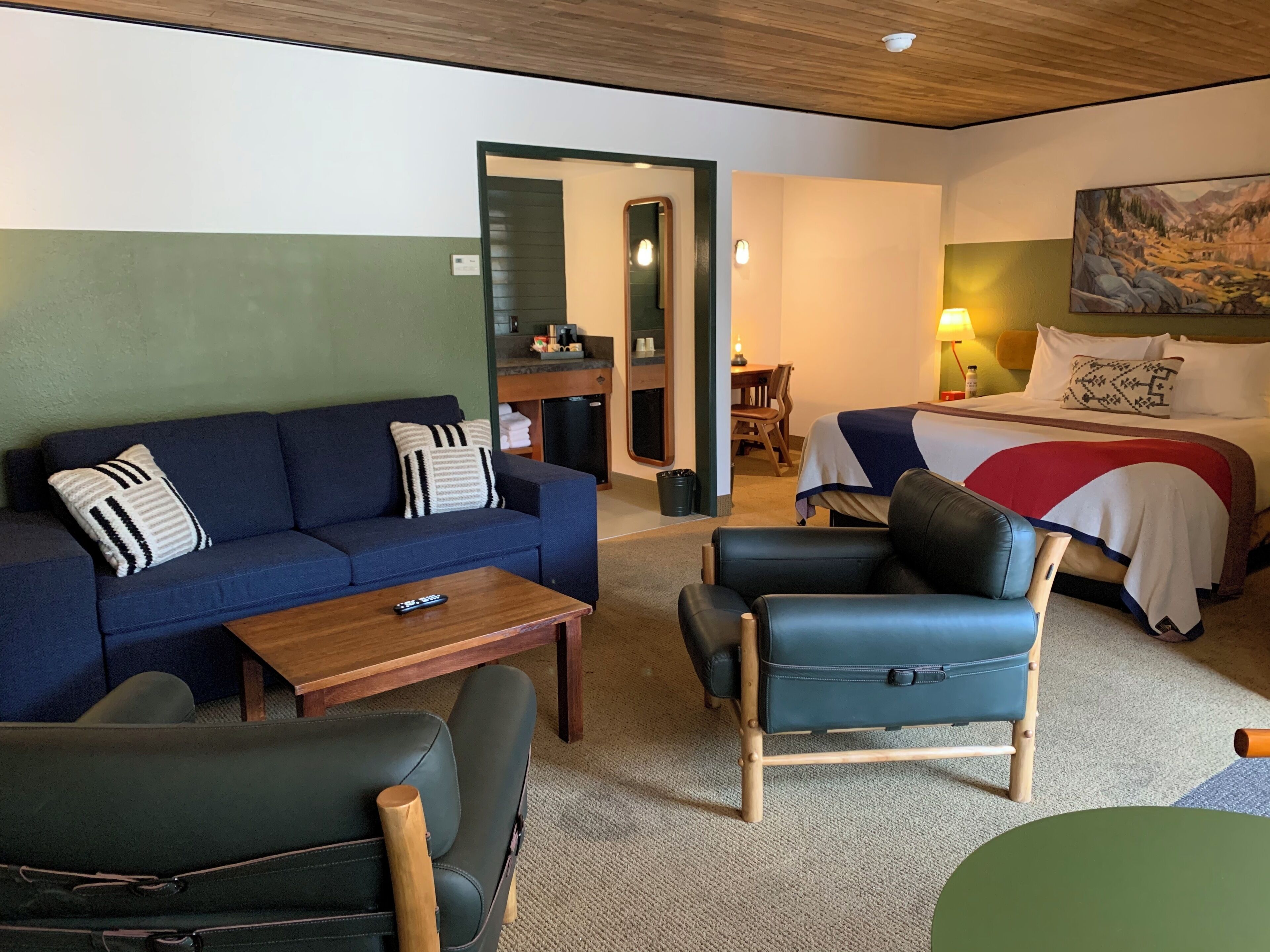 A room with a sofa, a chair, a bed, a small table, and a painting on the wall.
