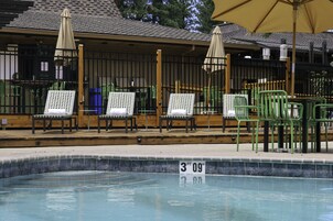 Ein Poolbereich mit Liegestühlen und Sonnenschirmen, eine Holzterrasse und ein eingezäunter Pool mit Tiefenmarkierung.