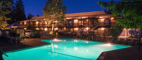 A hotel with a swimming pool, outdoor seating, and a well-lit building facade.