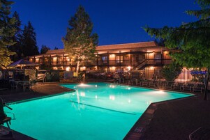 Un hotel con piscina, mobiliario exterior y fachada iluminada.