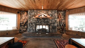 A cozy room with a stone fireplace, wooden ceiling, and large windows.