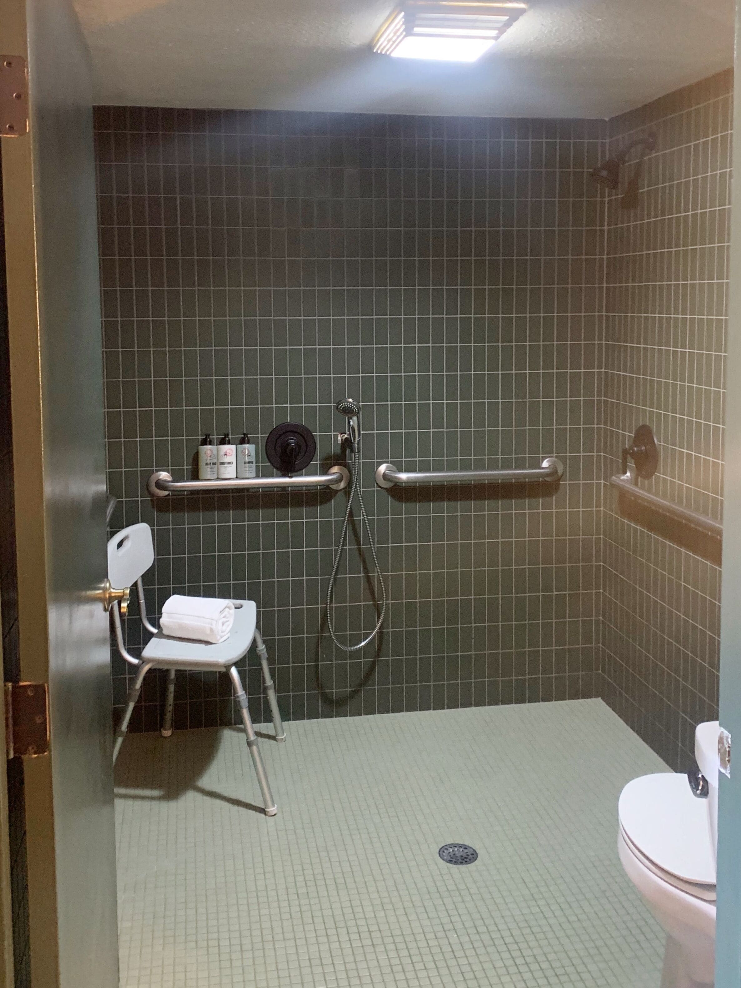 Un baño pequeño con azulejos, ducha, inodoro y una silla con toalla.