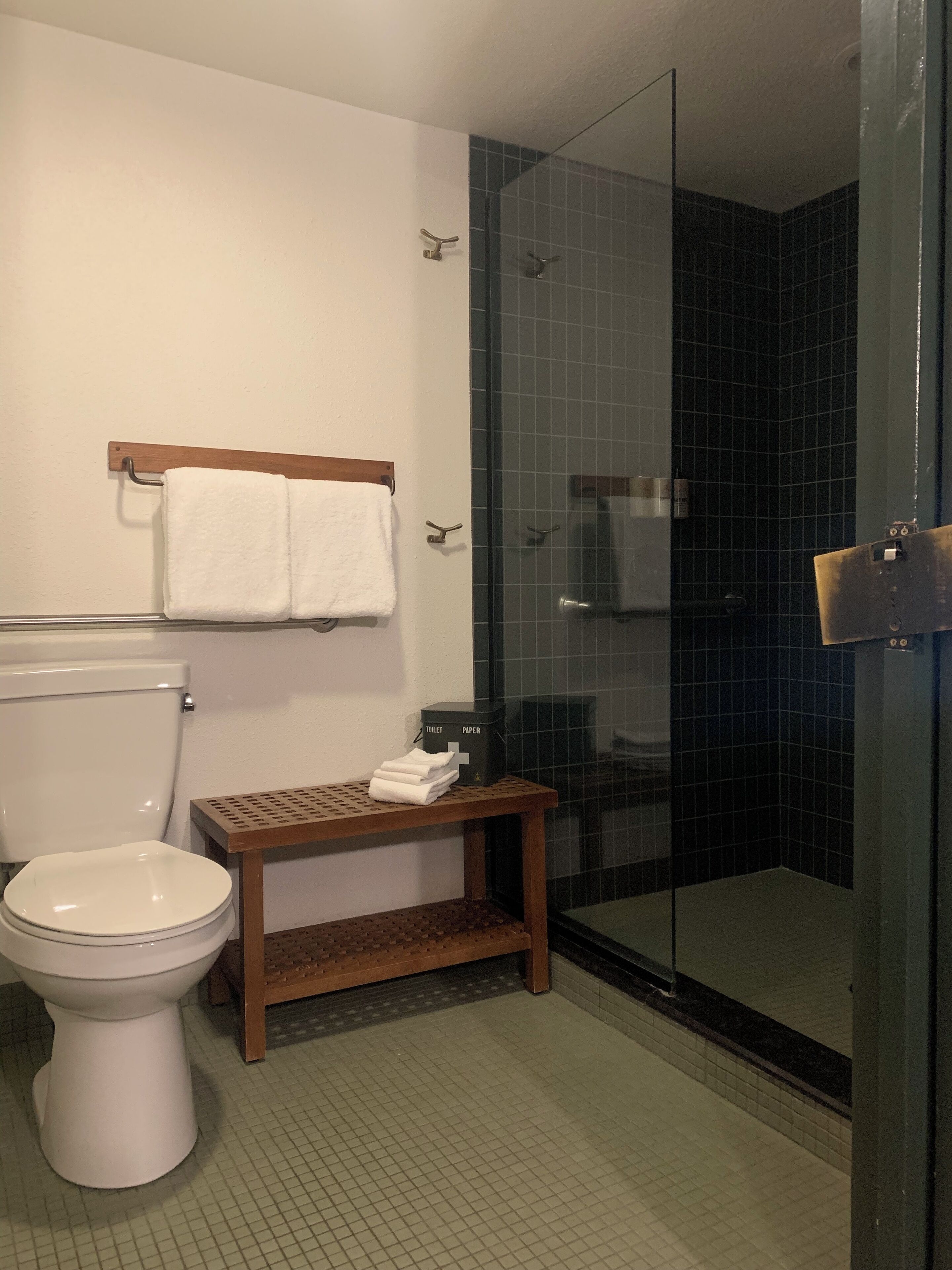 A bathroom with a toilet, a glass-enclosed shower, and a small wooden shelf with towels.