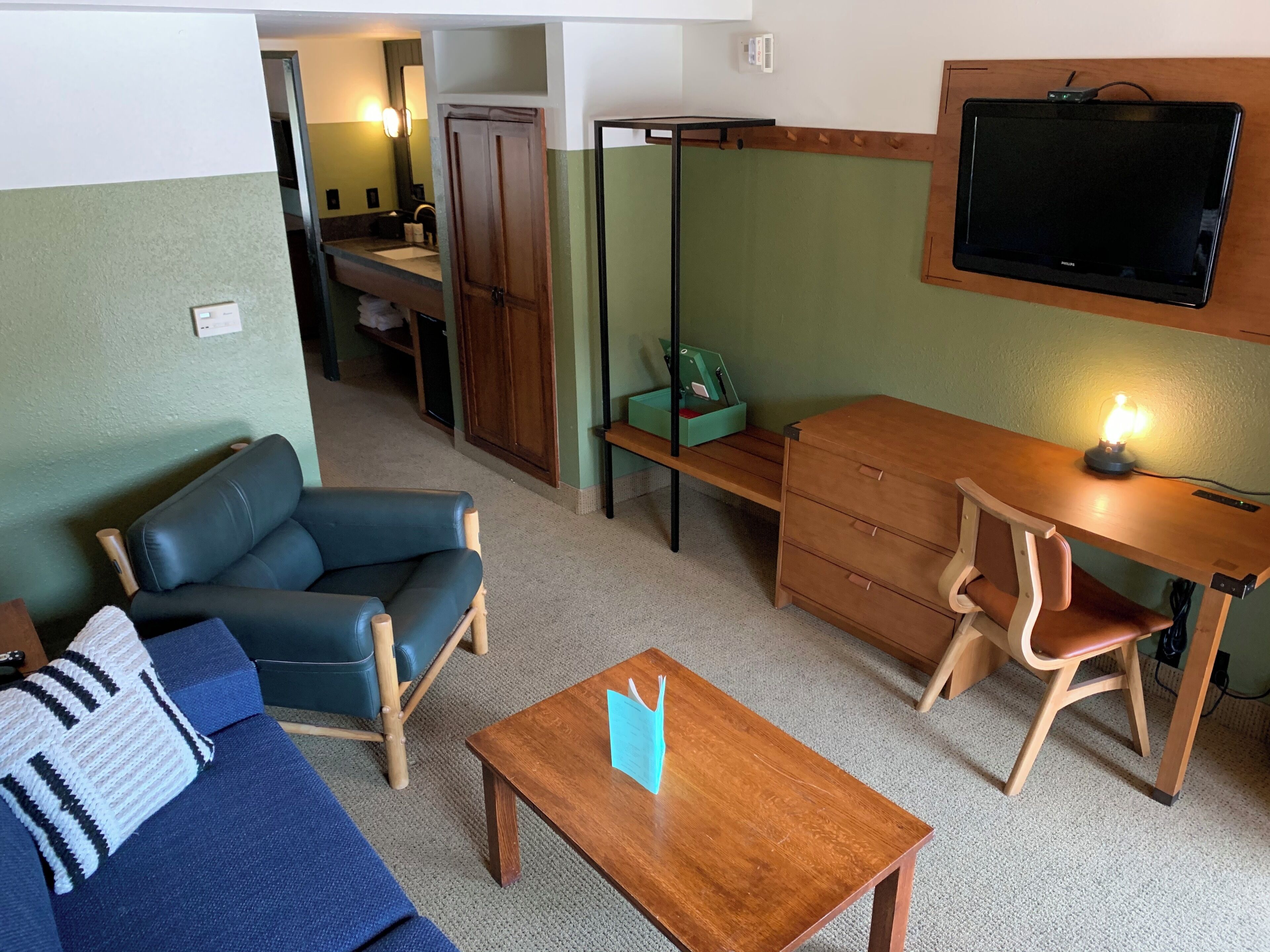 A room with a sofa, a wooden desk, a television, and a small table.