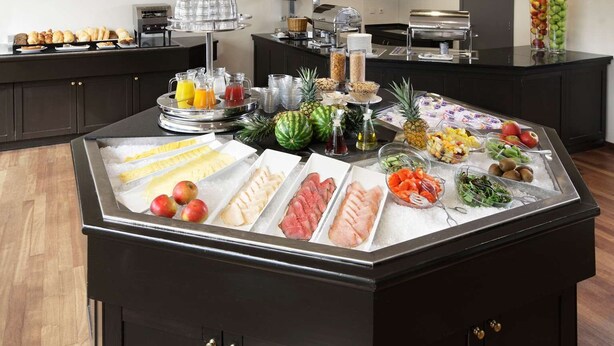 A buffet with various food items and beverages, including fruits, vegetables, and meats, displayed on a black counter. - NH Amsterdam Noord (Amsterdam)