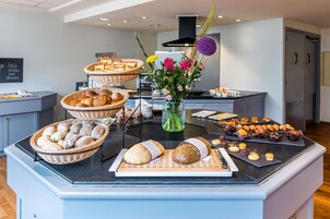 Un buffet proposant une variété de pains, de viennoiseries et agrémenté d’un vase de fleurs.