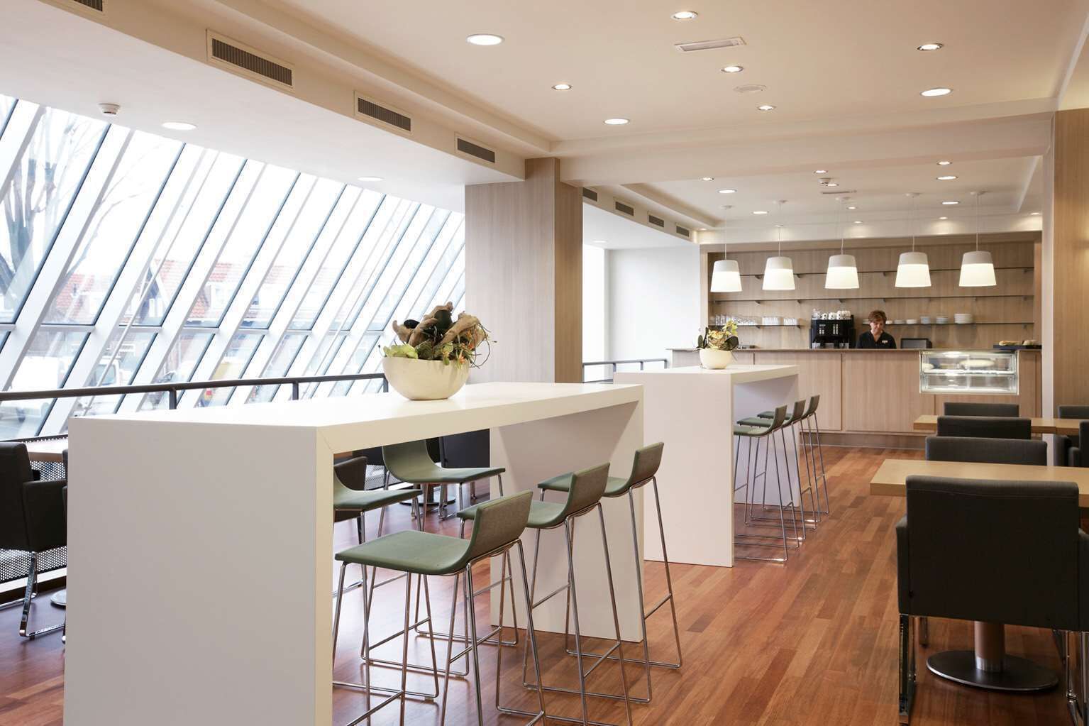 A modern bar area with high ceilings, a skylight, and a view of the city.