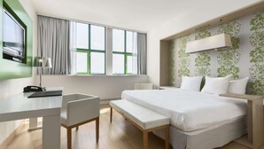 A modern hotel room with a large bed, a desk with a chair, a bench, and a TV mounted on the wall. - NH Amsterdam Noord (Amsterdam)