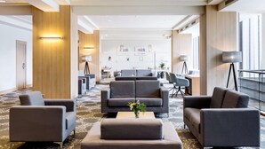 A spacious lobby with multiple seating areas, a reception desk, and artwork on the walls. - NH Amsterdam Noord (Amsterdam)