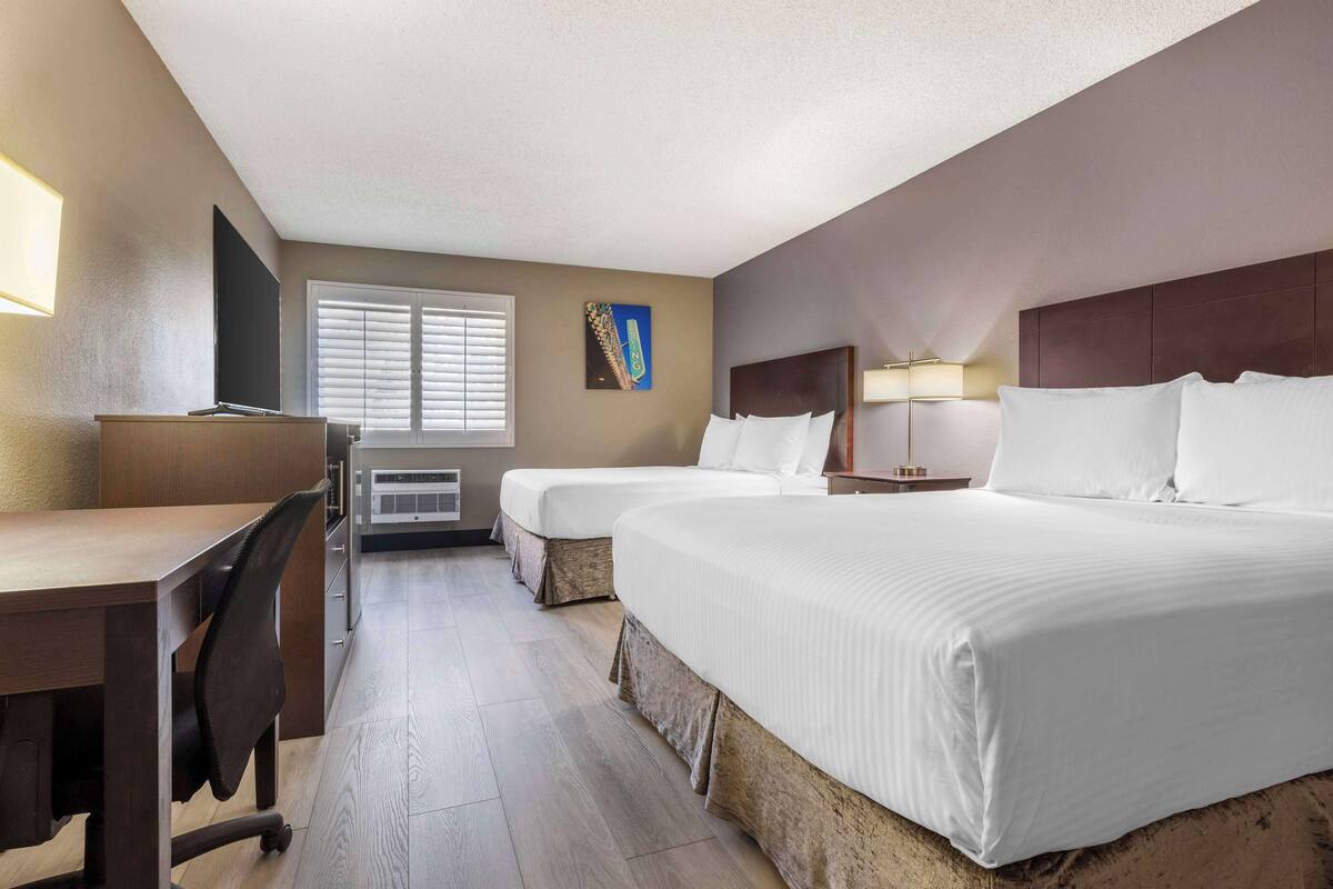 A hotel room with two beds, a desk, a chair, a TV, and a window with blinds.