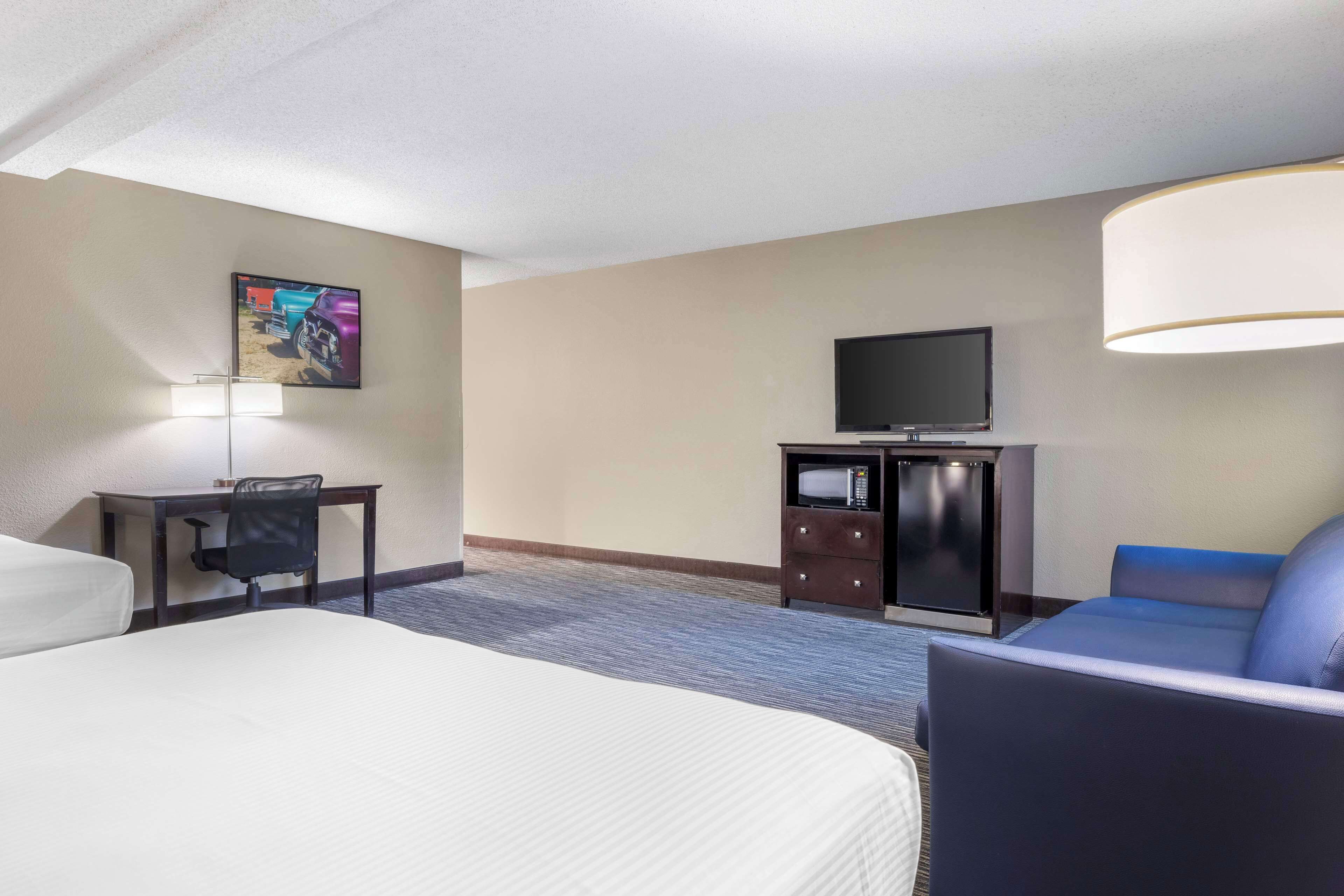 A hotel room with a bed, a desk, a chair, a television, and a couch.