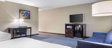 A hotel room with a bed, a desk, a chair, a television, and a couch.
