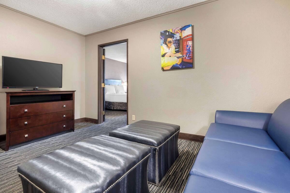 A hotel room with a flat-screen TV on a wooden cabinet, a blue sofa, and a small ottoman.