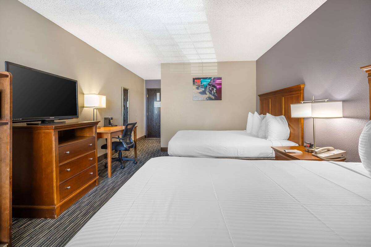 A hotel room with a large bed, a desk with a chair, a television, and a telephone.
