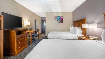 A hotel room with a large bed, a desk with a chair, a television, and a telephone.