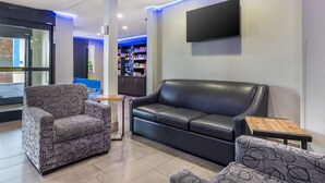 A modern lobby with a black leather sofa, patterned armchairs, and a flat-screen TV mounted on the wall. - Best Western McCarran Inn (Las Vegas)