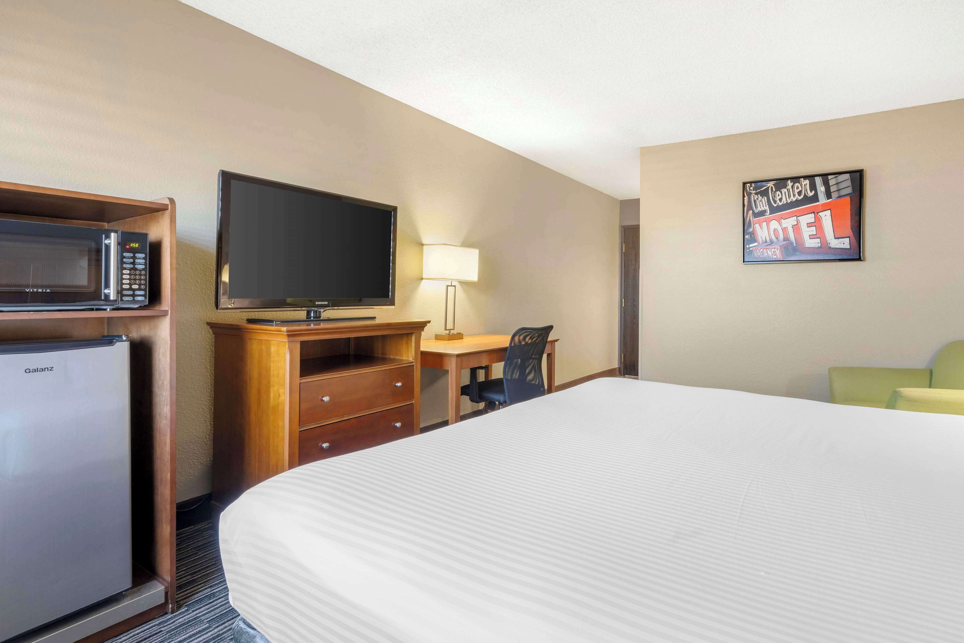 Quarto de hotel com cama, escrivaninha com cadeira, televisão, micro-ondas e frigorífico.