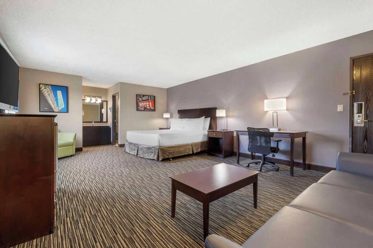 A hotel room with a bed, desk, chair, and a small table.