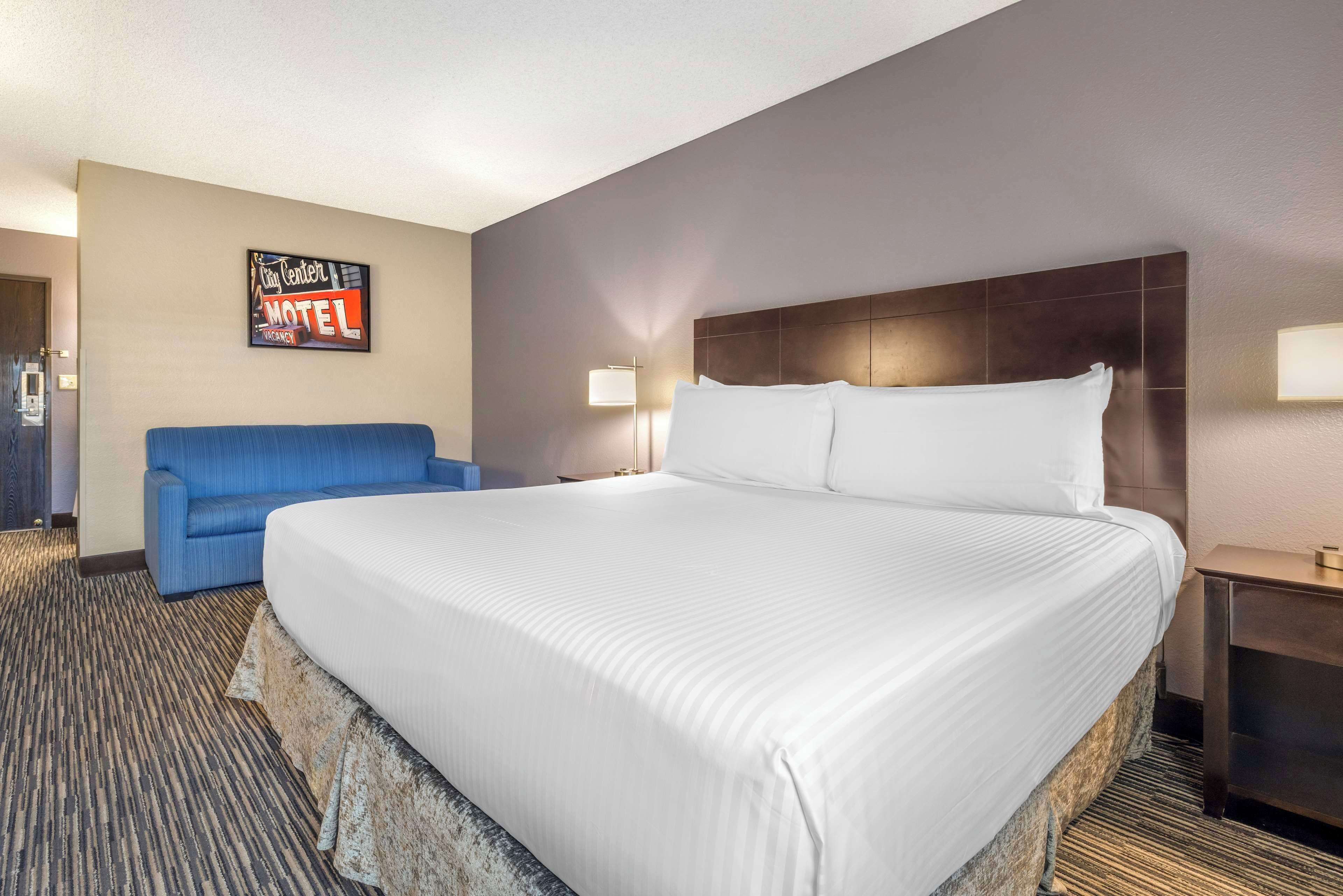 A hotel room with a large bed, a blue armchair, a nightstand, and a wall sign indicating it's a motel.