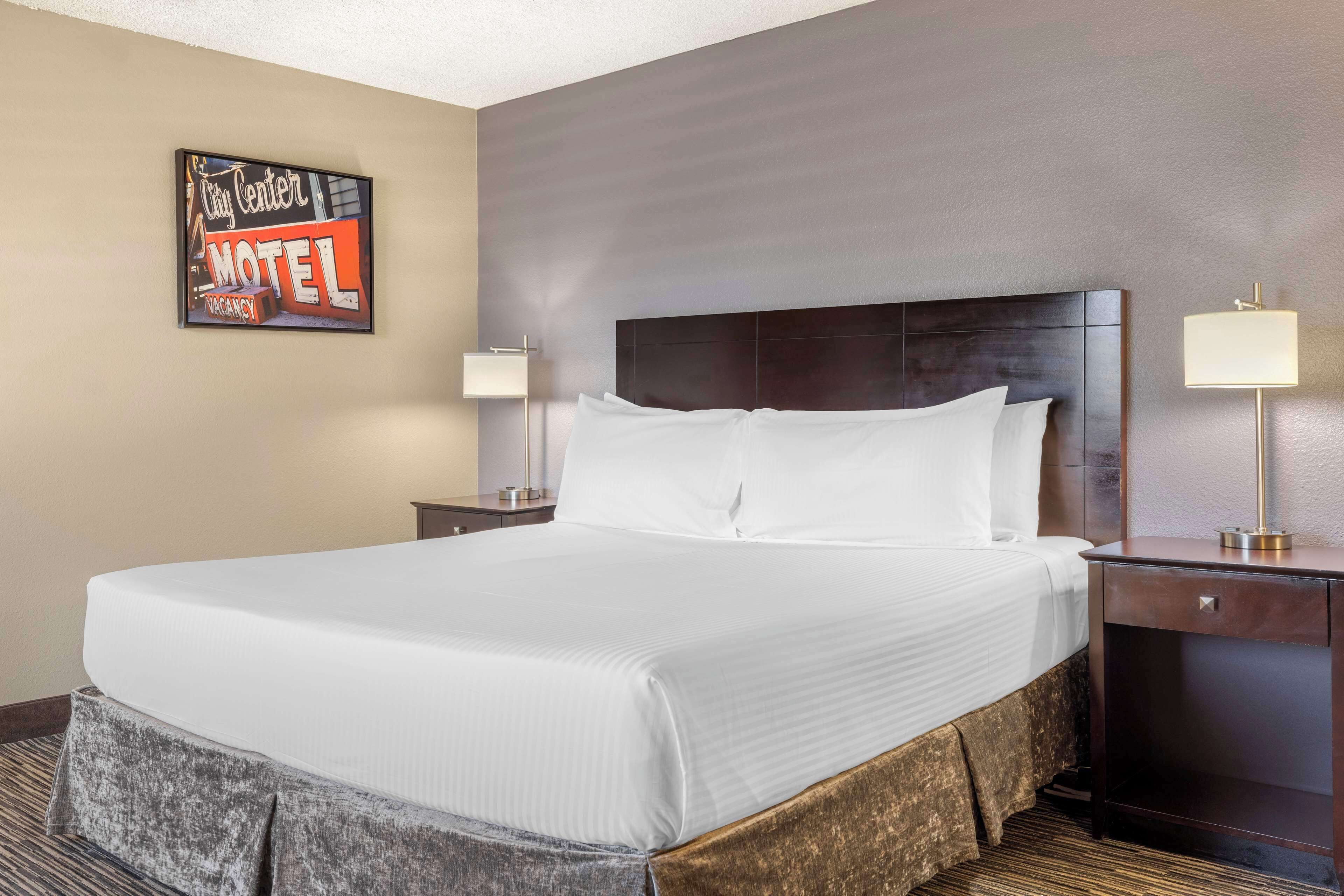 A hotel room with a large bed, two bedside tables, and a wall-mounted sign indicating a vacancy.