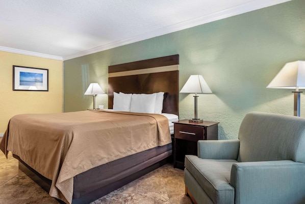 Una habitación de hotel con una cama, dos lámparas de noche, una silla y una mesita de noche.