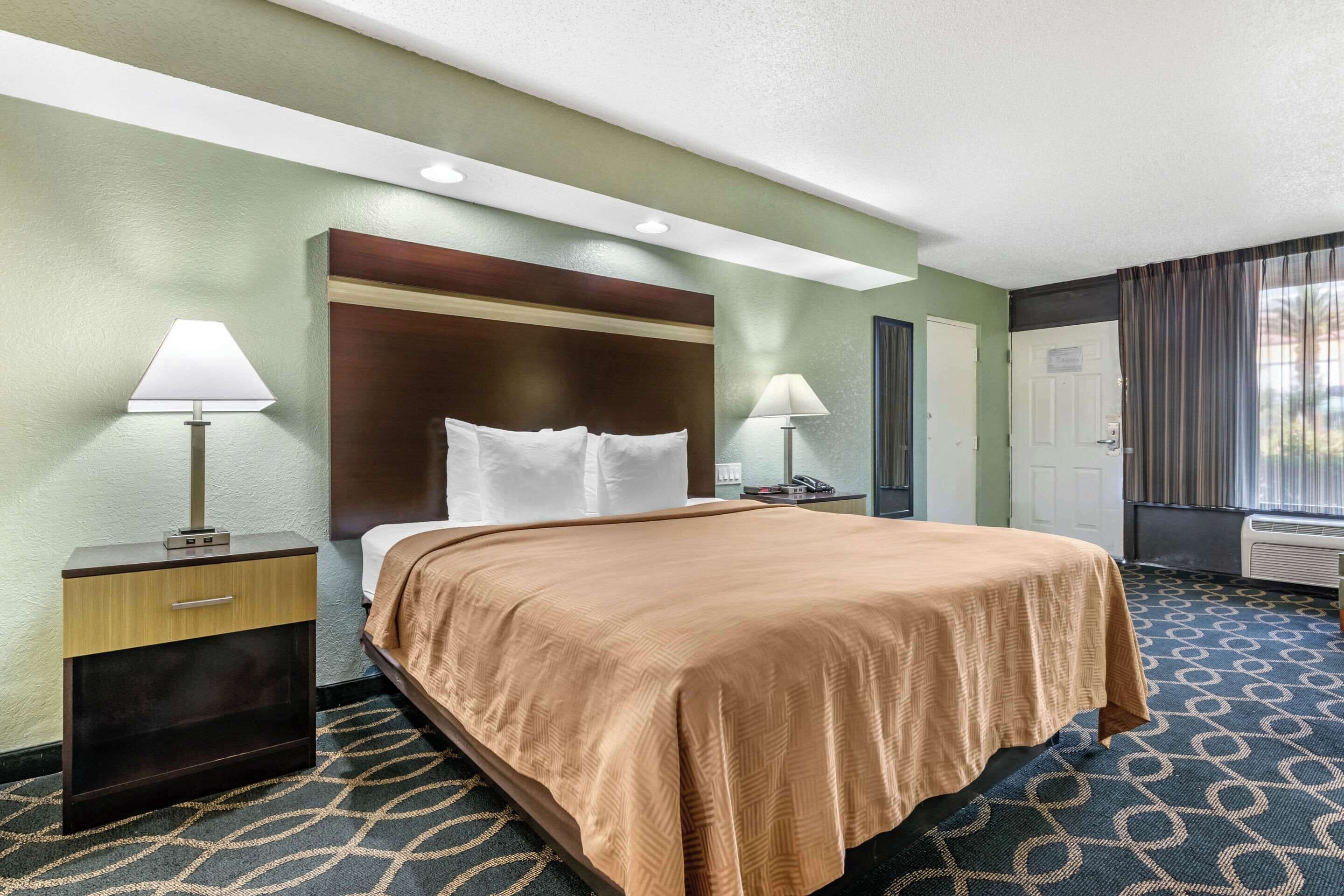 A hotel room with a bed, two bedside tables, a headboard, and a patterned carpet.