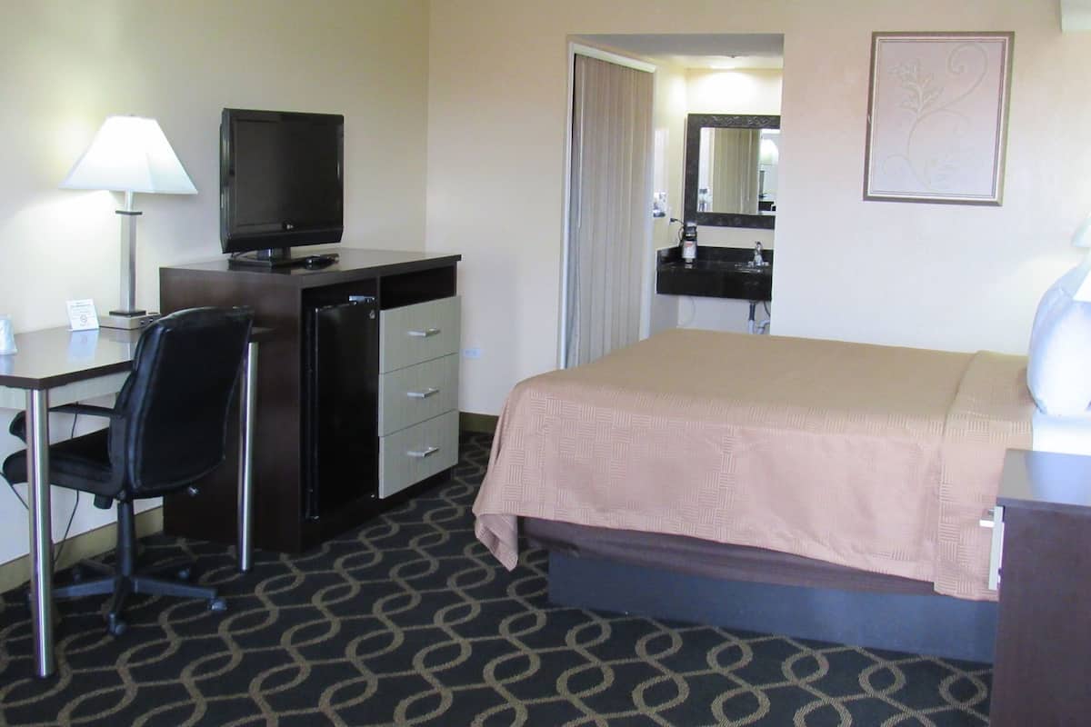 A hotel room with a bed, desk, chair, television, and a bathroom mirror.