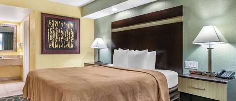 A hotel room with a large bed, a nightstand with a lamp, a mirror, and a decorative wall piece.