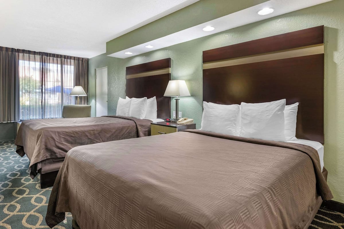 A hotel room with two beds, a nightstand with a lamp, a telephone, and a window with curtains.